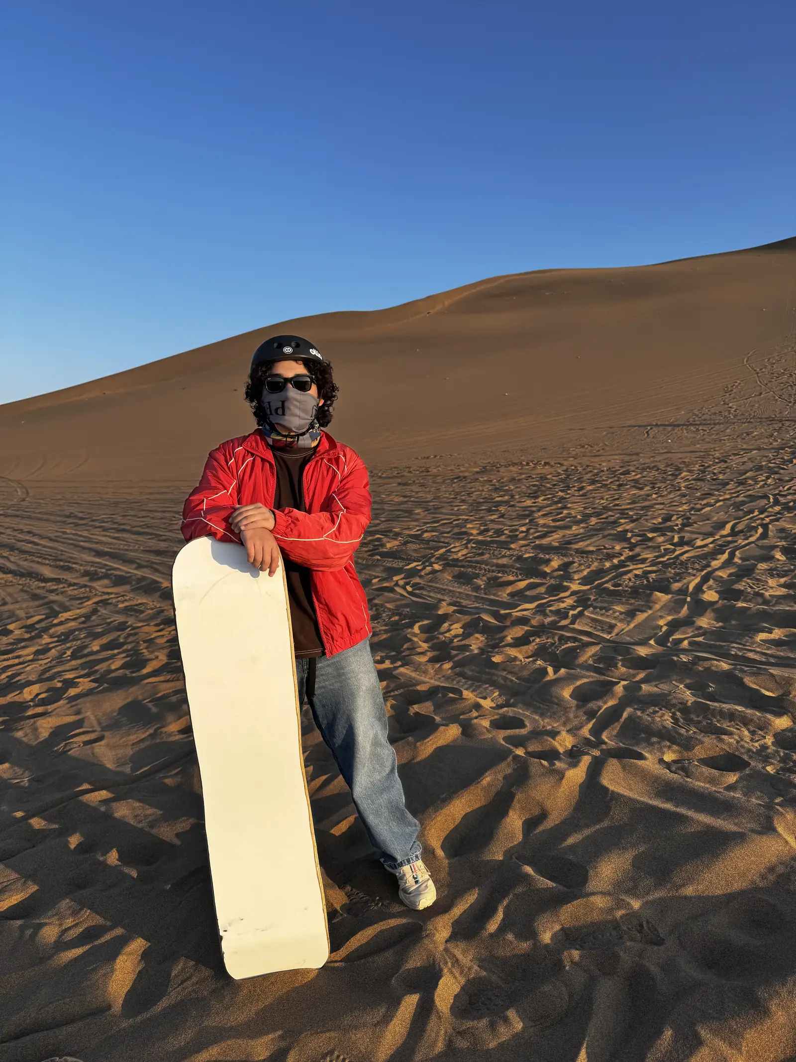 Yo, con casco y tabla de sandboard, sobre una duna de arena