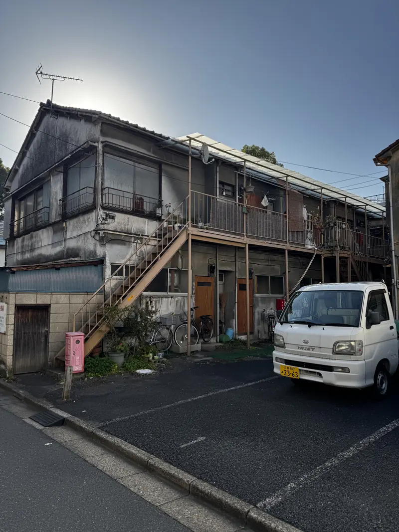 Una casa de madera de dos pisos y una camioneta pequeña en una calle tranquila, a contraluz