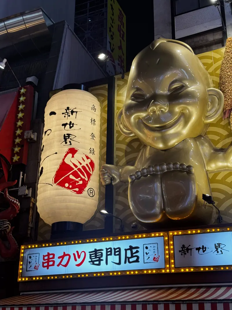 Un farol y una figura dorada sonriente en la entrada de un local de kushikatsu