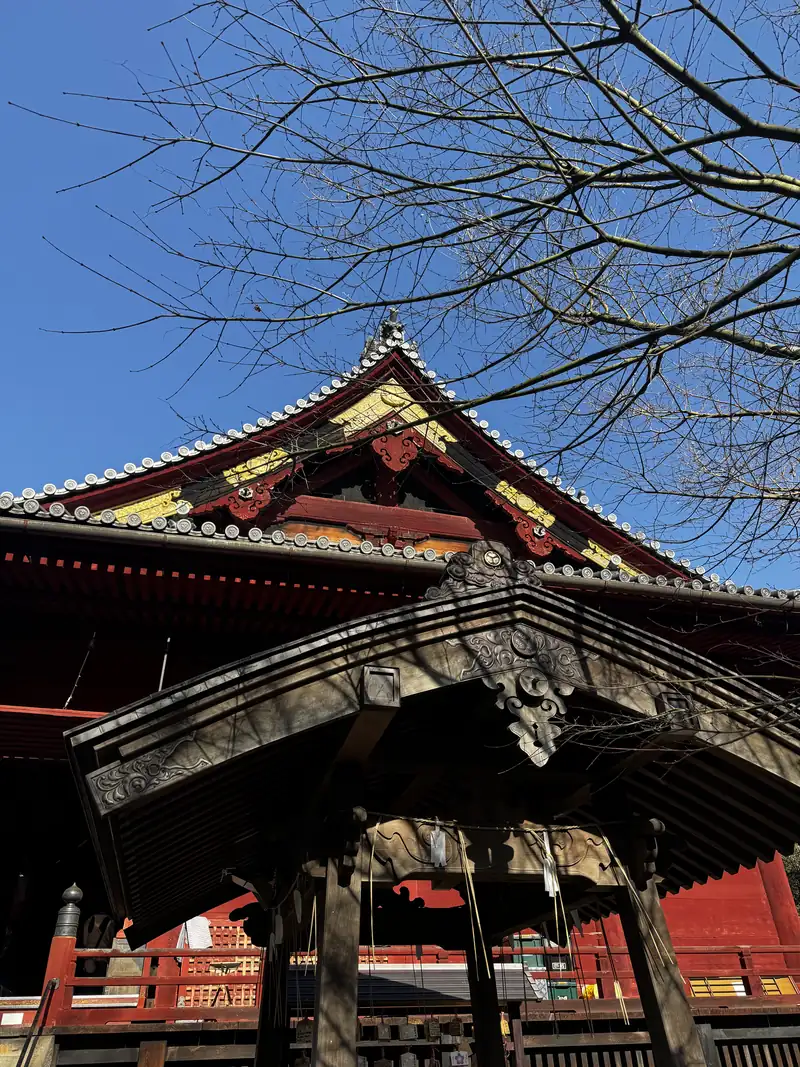 El alero decorado de un templo japonés contra el cielo azul, con ramas secas al frente